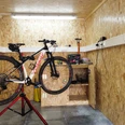 Fahrradgarage_Lüdenbach Fahrrad in einer Werkstatt auf einem Ständer, umgeben von OSB-Holzwänden und Werkzeugregalen.