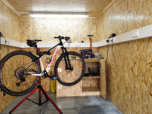 Fahrrad in einer Werkstatt auf einem Ständer, umgeben von OSB-Holzwänden und Werkzeugregalen.