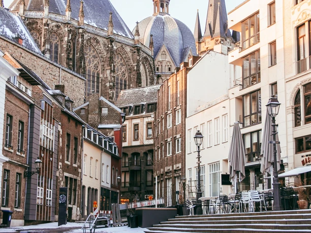 Ein verschneiter Innenhof in der Altstadt, umgeben von historischen Häuserreihen und dem Aachener Dom dahinter.