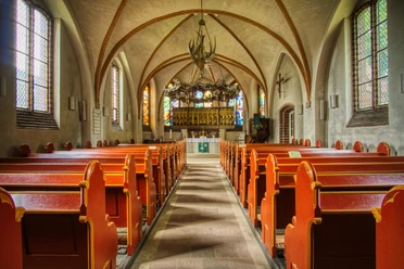 Innenansicht Kirchenschiff der St. Peter und Paul Kirche mit roten Holzbänken und goldenem Altar.