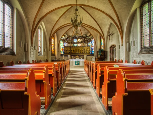 Innenansicht Kirchenschiff der St. Peter und Paul Kirche mit roten Holzbänken und goldenem Altar.