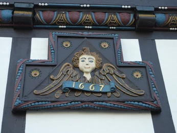 Holzgeschnitztes Engelsrelief an einem Fachwerkhaus, Jahr 1667, mit dekorativen Verzierungen.