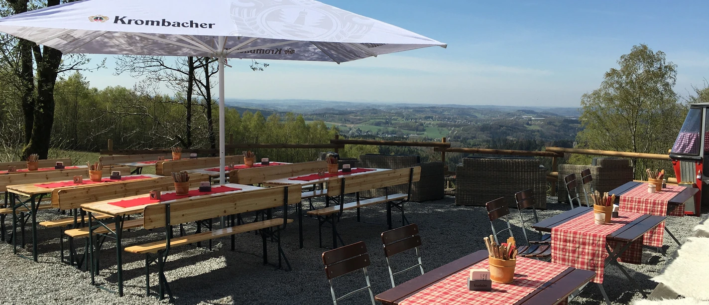 Panoramahütte am Blockhaus Panoramablick von einer Außenterrasse mit Holzbänken und -tischen, umgeben von grüner Landschaft.