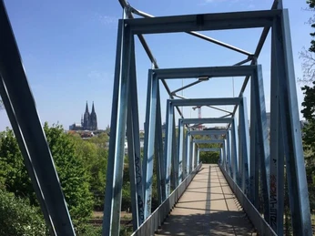 Locust bridge Stahlblaue Herkulesbrücke mit Blick auf den Kölner Dom, gesäumt von grünen Bäumen.Steel-blue Hercules Bridge with a view of Cologne Cathedral, lined with green trees.