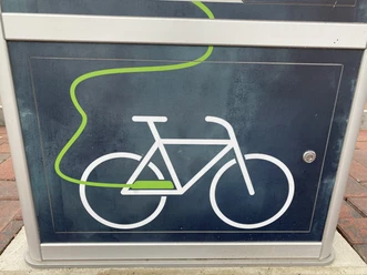 E-Bike-Ladestation Symbol eines Fahrrads mit grünem Kabel auf einer dunkelgrauen Ladestation für E-Bikes.