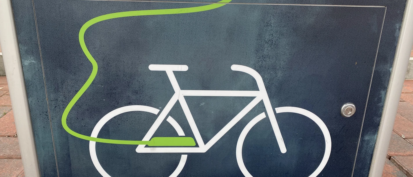 E-Bike-Ladestation Symbol eines Fahrrads mit grünem Kabel auf einer dunkelgrauen Ladestation für E-Bikes.