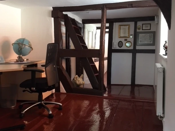 Arbeitszimmer in einem historischen Gebäude mit Holzbalken, Schreibtisch und Globus auf mattem Holzfußboden.