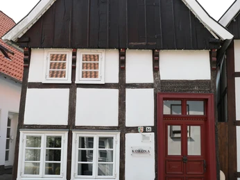 Fachwerkhaus mit Holz-Balken, rotem Giebel und Fensterläden; historische Optik, gepflasterter Weg.