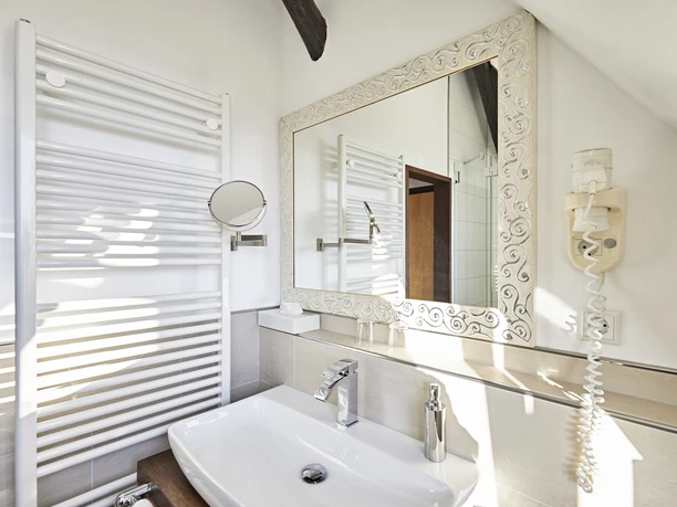 Spiegel im Bad mit elegantem Rahmen, darunter Waschbecken, Wandheizkörper und Haartrockner.