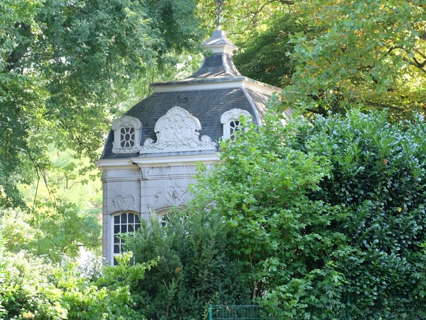 Kurpark Burtscheid Historisches Gebäude mit weißer Fassade und grauem Dach erscheint hinter einem dichten Baum.