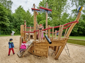 Piratenwelt Spielpark Wingst Kinder spielen auf einem hölzernen Piratenschiff im Sandspielbereich der Piratenwelt des Spielparks Wingst.