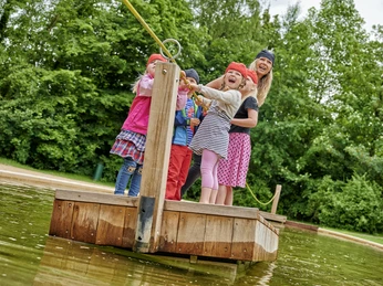 Spielpark Wingst Piratenwelt Kinder mit Piratenbändern überqueren lachend das Wasser auf einem Floß im Spielpark Wingst.