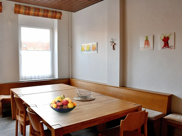 Großer Holztisch in einem schlichten, hellen Raum mit dekorativen Gemälden und einem Obstkorb.
