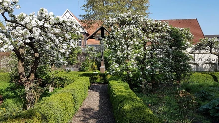 Ein blühender Garten mit grünen Hecken und einem malerischen Fachwerkhaus im Hintergrund.