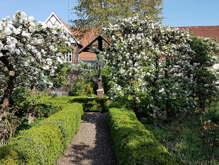 Kloster_Wiedenbrück_2.jpg Ein blühender Garten mit grünen Hecken und einem malerischen Fachwerkhaus im Hintergrund.