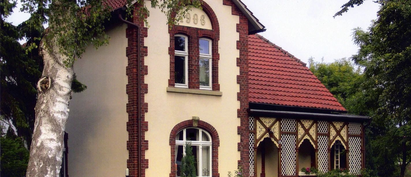 Historisches Backsteinhaus mit rotem Dach und verzierten Fenstern, umgeben von gepflegtem Garten.