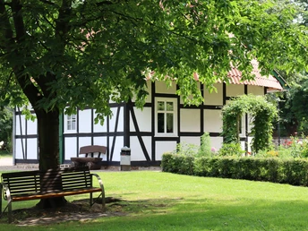 Fachwerkhaus im Kurpark Rothenuffeln, umgeben von Bäumen und einer gepflegten Grünfläche mit Bank.