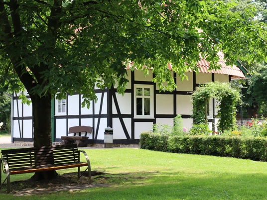 Fachwerkhaus im Kurpark Rothenuffeln, umgeben von Bäumen und einer gepflegten Grünfläche mit Bank.