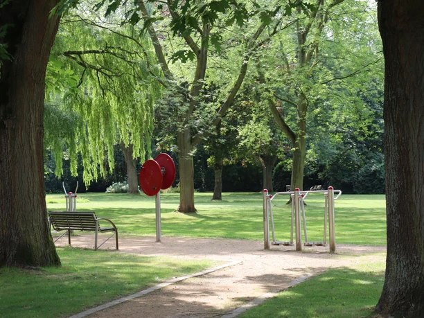 Kurpark Rothenuffeln Offener Parkbereich mit Fitnessgeräten, Bäumen und Sitzbank; rollstuhlgerecht angelegt.