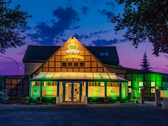 Eventhaus Schamin bei Sonnenuntergang, beleuchtet in Grün, mit Glasfassade und Fachwerkstruktur.