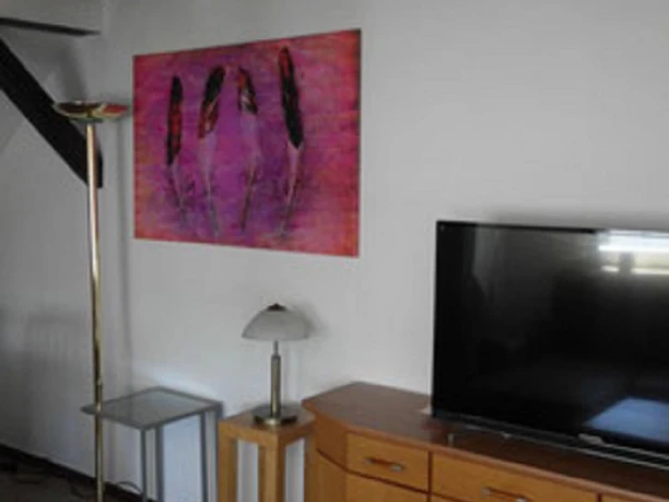 9.jpg Wohnzimmer mit Holzmöbeln, Flachbild-TV und bunter Kunst an der weißen Wand für einladende Atmosphäre.