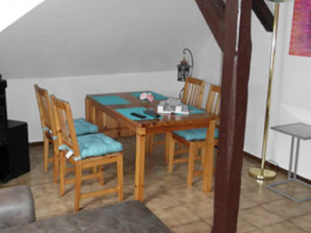 12.jpg Gemütliches Wohnzimmer in einer Dachwohnung mit Esstisch, vier Stühlen, Sofa und Holzbalken.