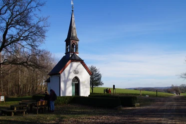 Germanakapelle Eine kleine weiße Kapelle mit schmalem Turm steht neben einem ruhigen Weg in ländlicher Umgebung.