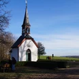 Germanakapelle Eine kleine weiße Kapelle mit schmalem Turm steht neben einem ruhigen Weg in ländlicher Umgebung.