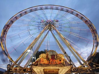 Ein beleuchtetes Riesenrad dreht sich bei Abenddämmerung, dessen helle Lichter den nächtlichen Himmel erhellen.