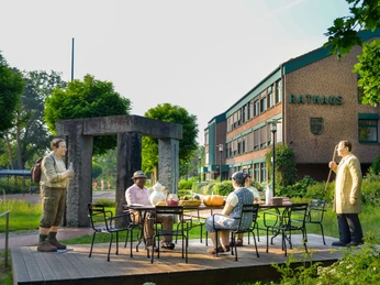 Fünf Figuren von Christel Lechner an einer Kaffeetafel auf einem Podest vor dem Rathaus stellen Typisches für die Ortsteile dar