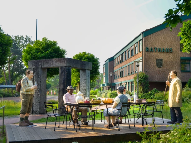 Fünf Figuren von Christel Lechner an einer Kaffeetafel auf einem Podest vor dem Rathaus stellen Typisches für die Ortsteile dar Fünf Figuren von Christel Lechner an einer Kaffeetafel auf einem Podest vor dem Rathaus stellen Typisches für die Ortsteile dar