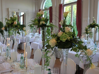 spiegelsaal-tischdeko-hochzeit.jpg Festlich gedeckter Hochzeitstisch im prächtigen Spiegelsaal mit eleganten Blumenarrangements aus weißen Rosen und Kerzen.