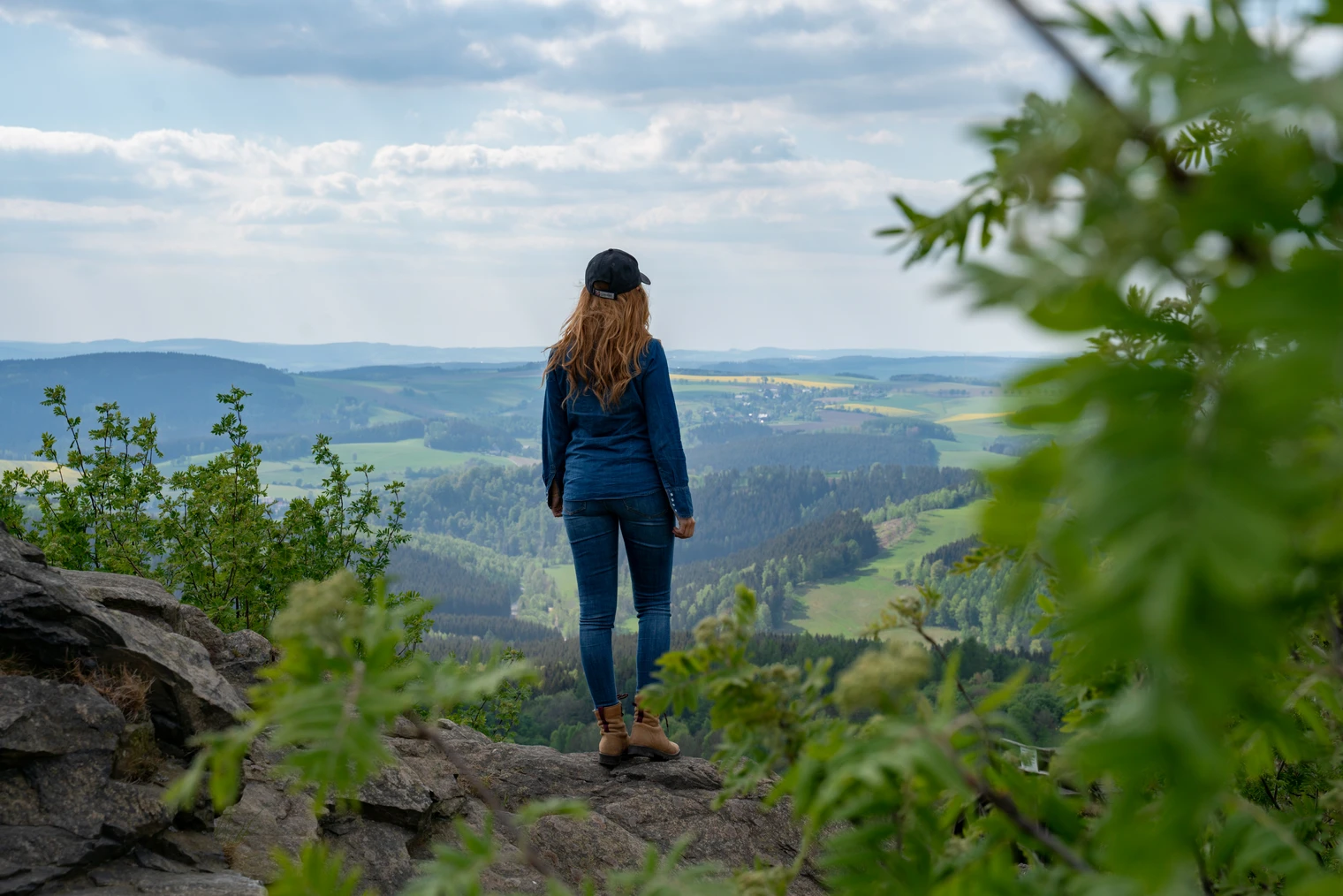 Am Schwartenberg (c) Thorsten Günthert (4).jpg Eine Frau steht auf einem Felsen und blickt über eine weite, grüne Hügellandschaft.