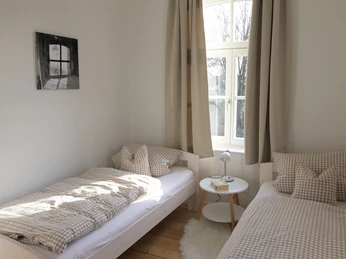 Kuesterhaus_1.JPG Helles Zimmer mit zwei Einzelbetten, karierten Bettdecken und einem großen Fenster mit Tageslicht.