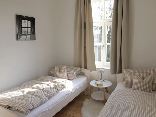 Kuesterhaus_1.JPG Helles Zimmer mit zwei Einzelbetten, karierten Bettdecken und einem großen Fenster mit Tageslicht.