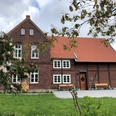 Kuesterhaus_2.JPG Backstein- und Fachwerkgebäude mit rotem Ziegeldach, umgeben von grüner Wiese und blühenden Bäumen.