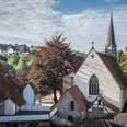 St. Stephan Kirche mit gotischem Turm, umgeben von grünen Bäumen und traditionellen Häusern.