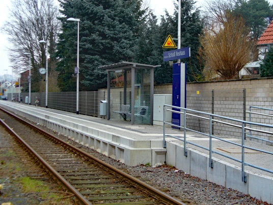 Bahnhof Schloß Neuhaus Ein kleiner Bahnhof mit modernem Wartebereich, Geländer, Bäumen und einem Weg entlang der Gleise.