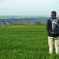 Aussichtspunkt Papenberg Mann im Grünen, blickt auf weite Landschaft mit Feldern, Ortschaft und Windrädern im Hintergrund.