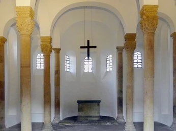 Rundbögen und Säulen umranden den Altarraum der Bartholomäuskapelle, betont durch schlichtes Kreuz.