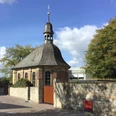 Alexiuskapelle Alexiuskapelle in Paderborn: Backsteingebäude mit rundem Dach und Turm, umgeben von Bäumen im Sonnenschein.