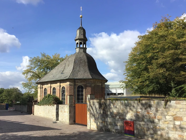 Alexiuskapelle Alexiuskapelle in Paderborn: Backsteingebäude mit rundem Dach und Turm, umgeben von Bäumen im Sonnenschein.