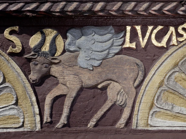 Flachrelief eines geflügelten Stiers mit goldener Inschrift "S. LVCAS" auf einem Fachwerkhaus.