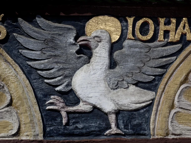 Steinrelief eines Vogels mit goldener Aura, umgeben von vergoldeten Buchstaben auf dunklem Hintergrund.