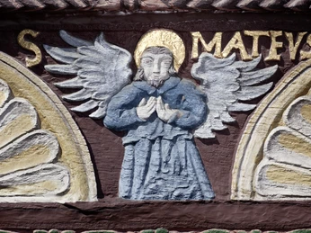 Ein kunstvoll geschnitzter Engel mit goldenem Heiligenschein und detaillierten Flügeln verziert eine Fachwerkfassade.