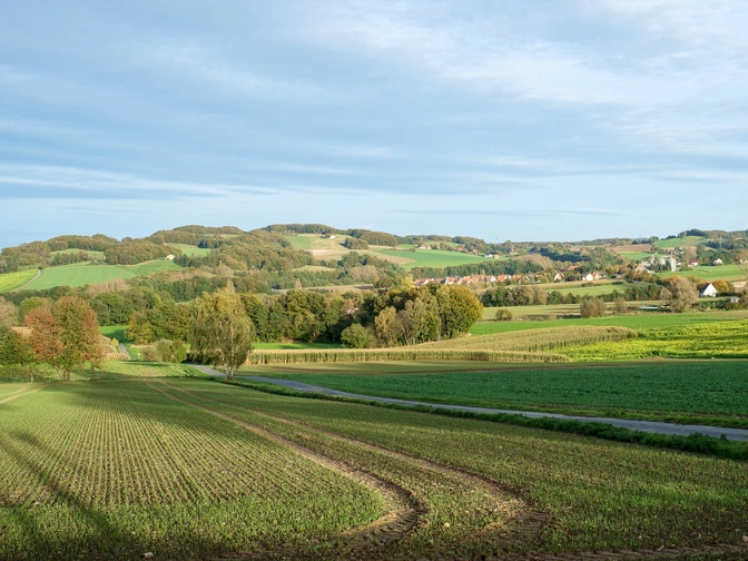 Ausblick Bonstapel Weite Felder unter blauem Himmel, sanfte Hügel im Hintergrund, vereinzelte Bäume und Häuser.