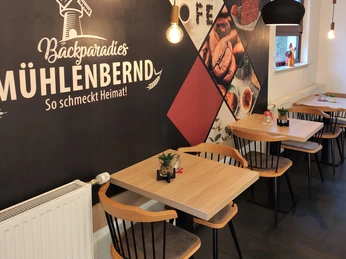 3 Tische mit 2 Sitzplätzen und dem Mühlenbernd Logo im Hintergrund