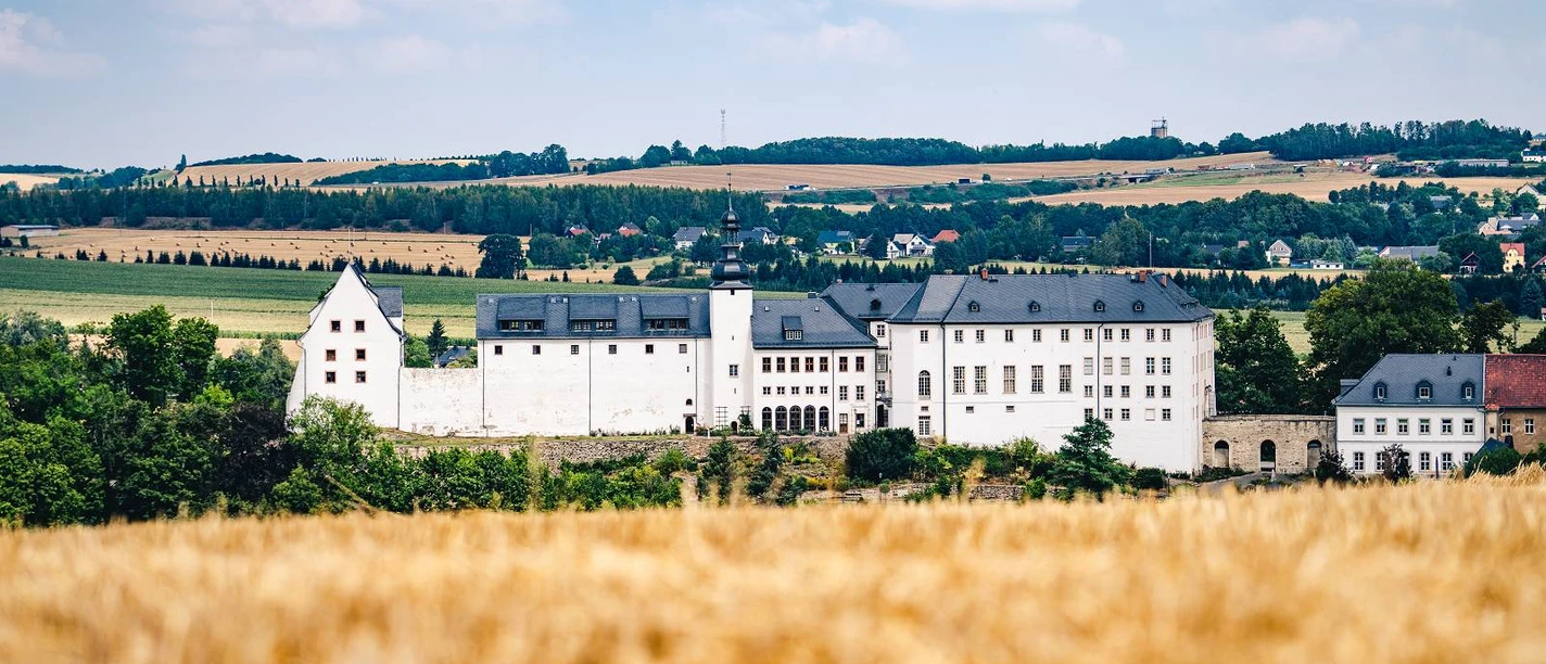 Schloss Wildenfels (C) Oliver Göhler_(1600_x_1200).jpg Schloss Wildenfels thront vor einer goldenen Getreidefeldkulisse unter blauem Himmel.