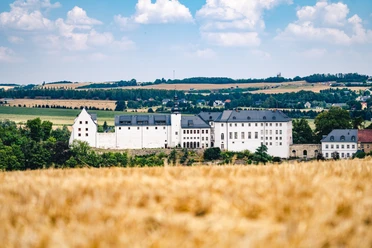 Schloss Wildenfels Il castello di Wildenfels con la sua facciata bianca e il tetto di ardesia, circondato da campi e colline dorate.