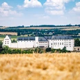 Schloss Wildenfels Schloss Wildenfels mit weißer Fassade und Schieferdach, umgeben von goldenen Feldern und Hügeln.Wildenfels Castle with its white façade and slate roof, surrounded by golden fields and hills.Zámek Wildenfels s bílou fasádou a břidlicovou střechou, obklopený zlatými poli a kopci.Zamek Wildenfels z białą fasadą i łupkowym dachem, otoczony złotymi polami i wzgórzami.Kasteel Wildenfels met zijn witte gevel en leistenen dak, omringd door gouden velden en heuvels.Il castello di Wildenfels con la sua facciata bianca e il tetto di ardesia, circondato da campi e colline dorate.